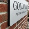 ADA Signs / Wayfinding 9 Custom exterior property identification sign with rounded corners and brushed silver finish mounted on a red brick wall displaying a property management company name