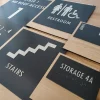 ADA Signs / Wayfinding 1 Multiple ADA compliant signs with Braille text and tactile lettering arranged on a light wood backer, including stairwell directional, restroom, unit number, stairs, and storage signs