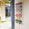 ADA Signs / Wayfinding 7 A unique custom decorative directional sign display featuring multiple colorful arrow-shaped signs on a wooden post, each styled as a vintage storefront name, installed in a themed interior space