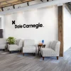 Dimensional Letters 2 Corporate office reception area with black dimensional letter logo sign on a white textured tile wall above a seating area with neutral upholstered chairs and reclaimed wood accents
